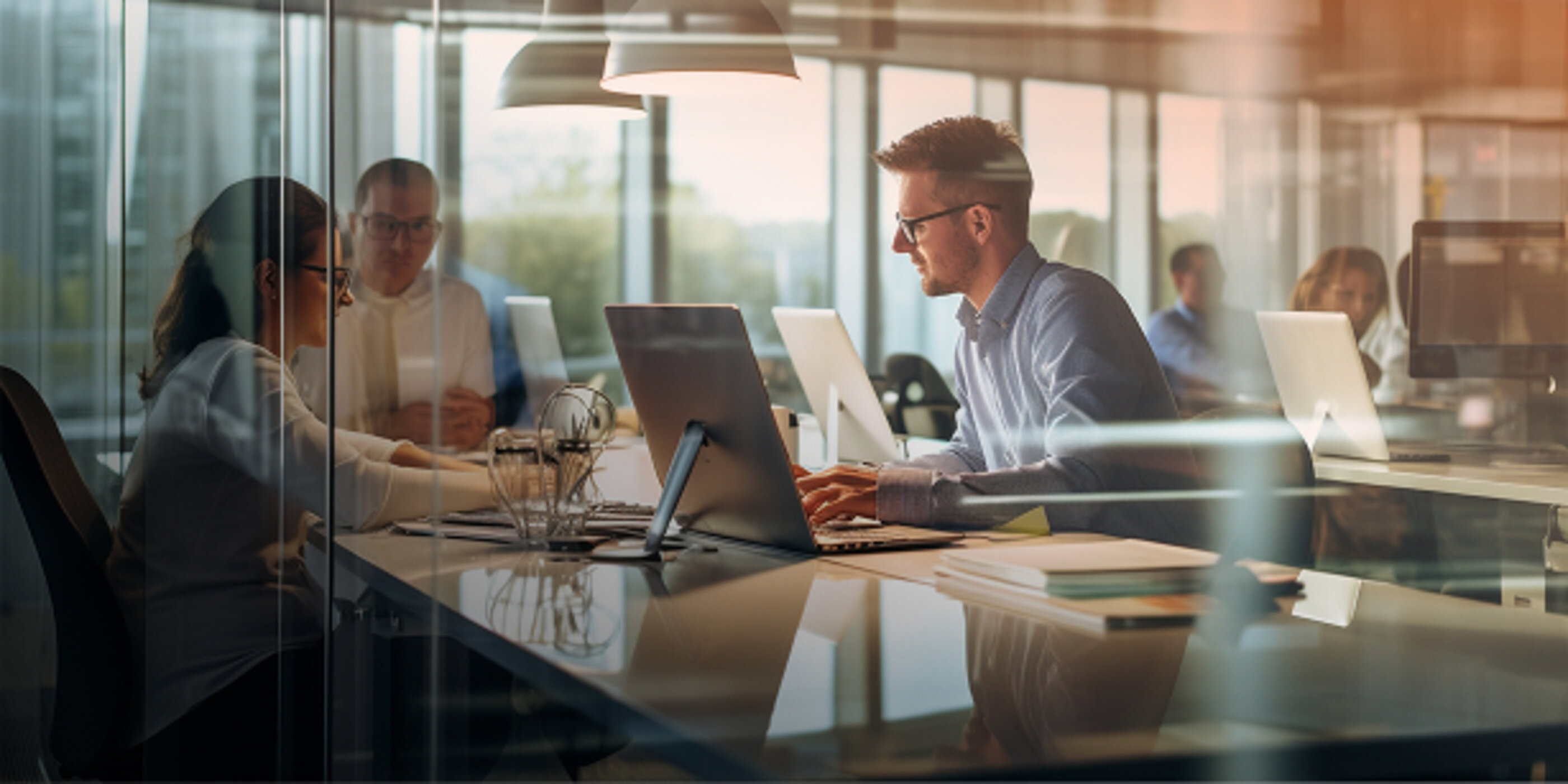 Mitarbeitende bei der Zusammenarbeit an Computern in einem modernen Büro mit Glaswänden